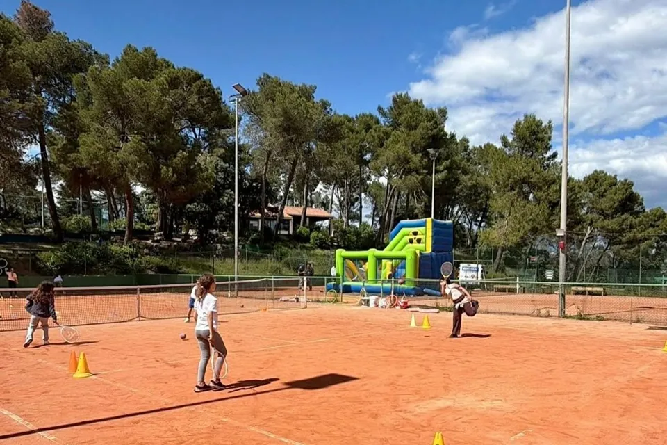 Courts en terre battue sous les pins, avec quelques joueurs à l'entraînement, ciel bleu