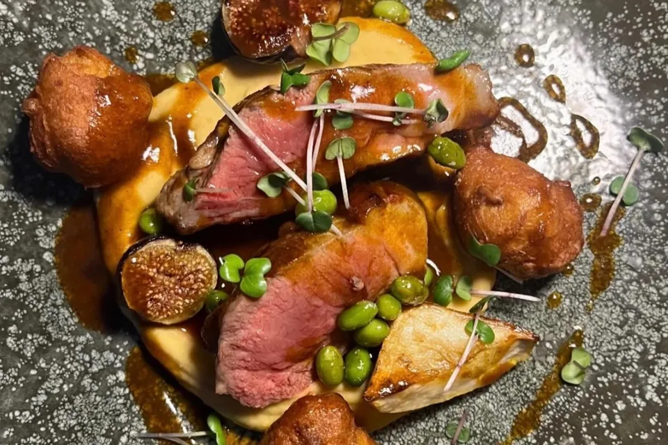 Une assiette de viande rosée tranchée, petits pois, figues et pommes dauphines sur une assiette grise mouchetée