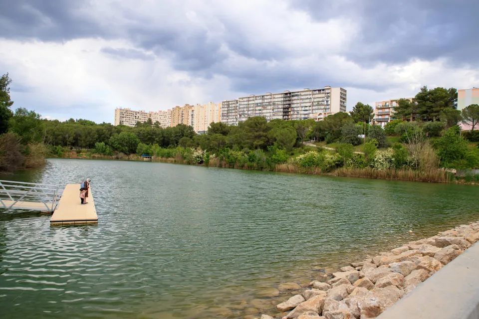 Le lac des Garrigues, son ponton et ses berges en enrochement, immeubles des Hauts de Massane à l'arrière