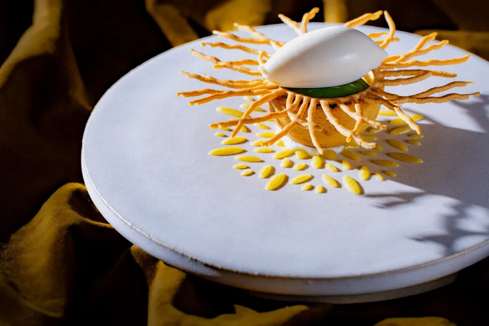 Un dessert blanc et jaune en couronne sur une assiette blanche, photographié sur fond sombre