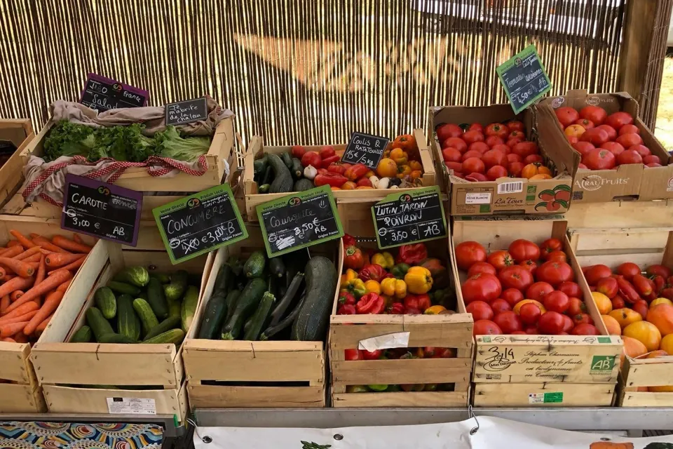 Le stand de la ferme, cagettes de tomates, courgettes, carottes et poivrons avec leurs ardoises, sous une canisse
