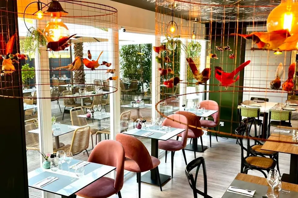 La salle du restaurant, tables dressées, suspensions lumineuses et grande baie vitrée
