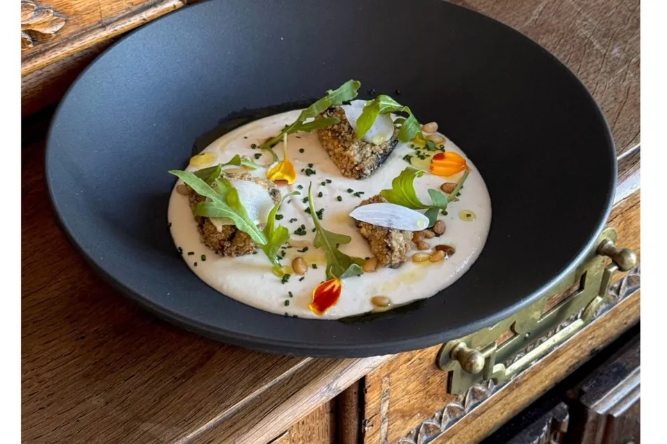 Une assiette gastronomique dans une assiette creuse noire, posée sur un meuble en bois sculpté