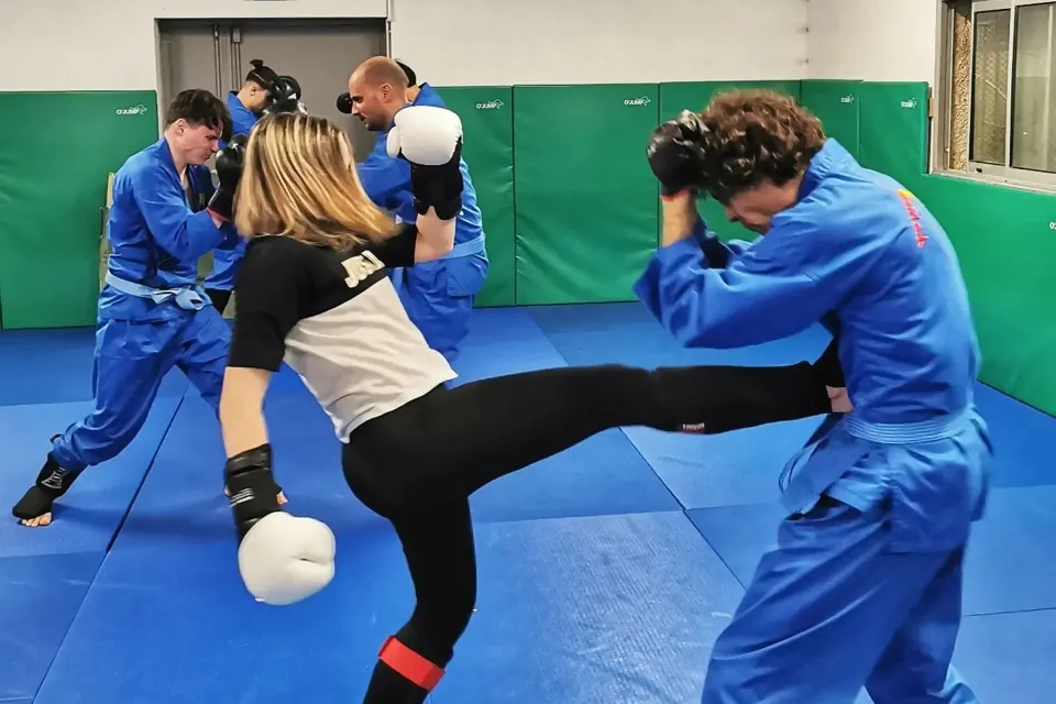 Entraînement sur tatami, une pratiquante gantée lance un coup de pied face à un partenaire en tenue bleue de Vovinam